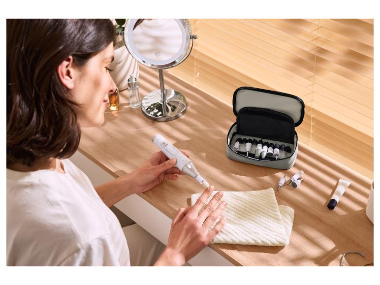 Vrouw gebruikt elektrische nagelvijl met manicure set op houten tafel.