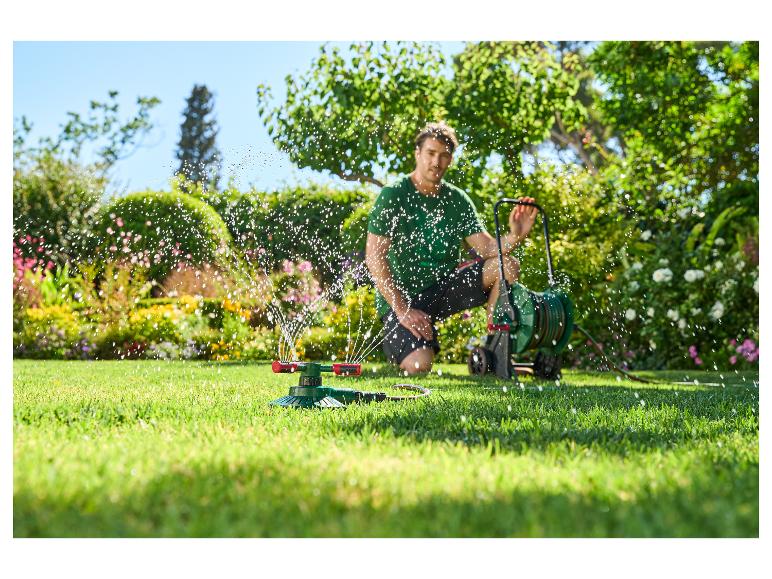 Man in een tuin met tuinslang en sproeier, besproeit het gazon.