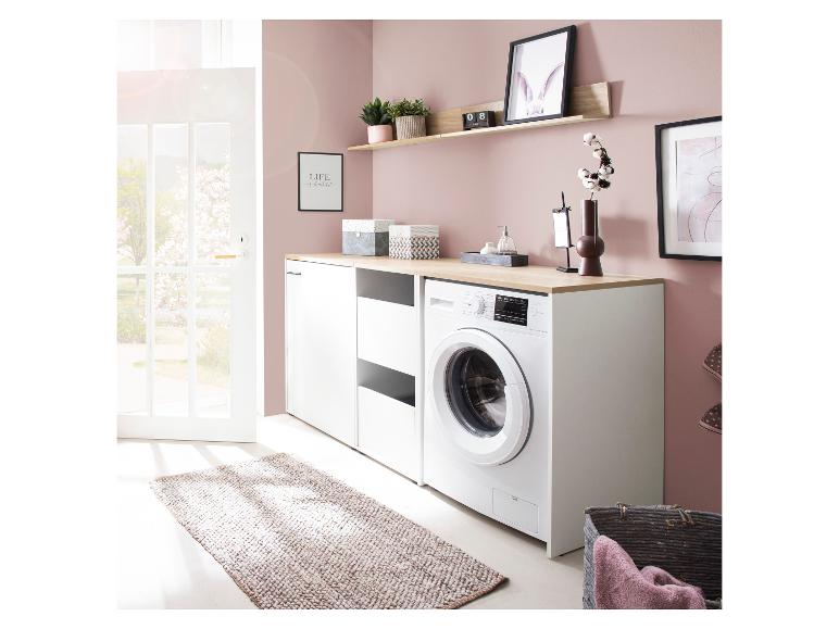 Wasmachine en kasten in wasruimte, roze muur, houten plank en raam met uitzicht naar buiten.