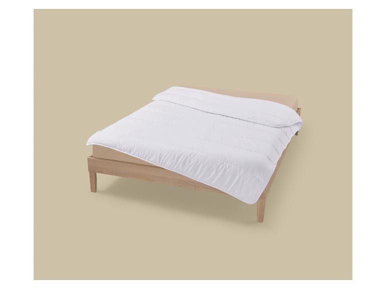 Wit dekbed op een houten bed met een beige hoeslaken.