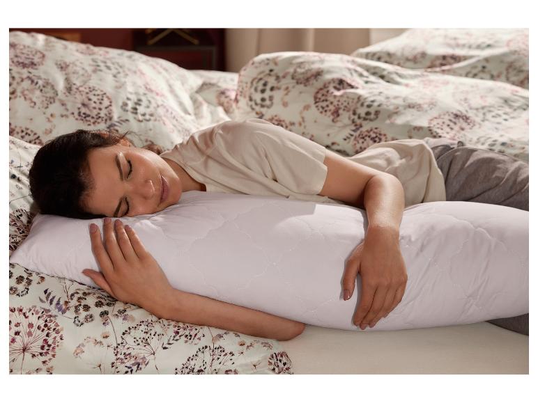 Vrouw slaapt in bed en omhelst een wit LIVARNO home zijliggingskussen.