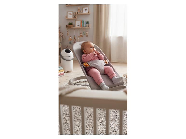 Baby in een grijze stoffen wipstoel in een kinderkamer met houten planken en decoratie.