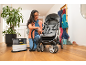 Een vrouw reinigt een kinderwagen op een houten vloer met een tapijtreiniger.