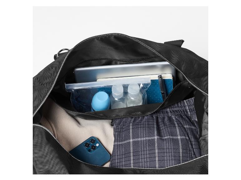 Open zwarte tas met tablet, toiletartikelen, notitieboekje, pen, telefoon en kleding.