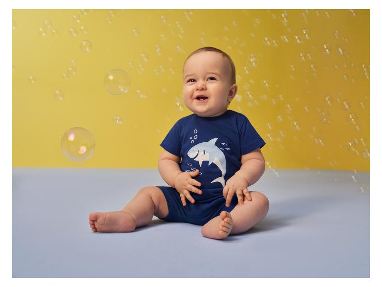 Lachende baby in blauwe haaienromper, omringd door bellen.
