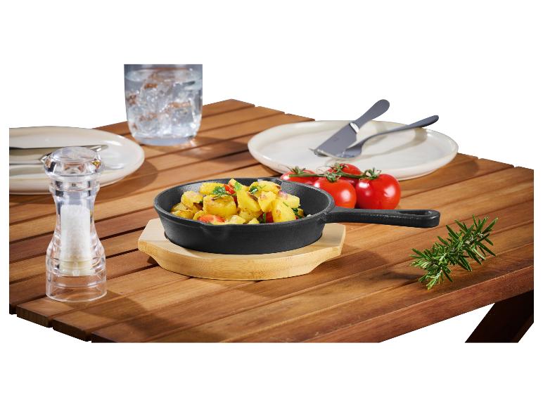 Gietijzeren pan met gebakken aardappelen, zout, tomaten en rozemarijn op een houten tafel.