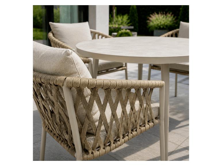 Buiten eethoek met ronde tafel en gevlochten stoelen met lichte kussens op een terras.