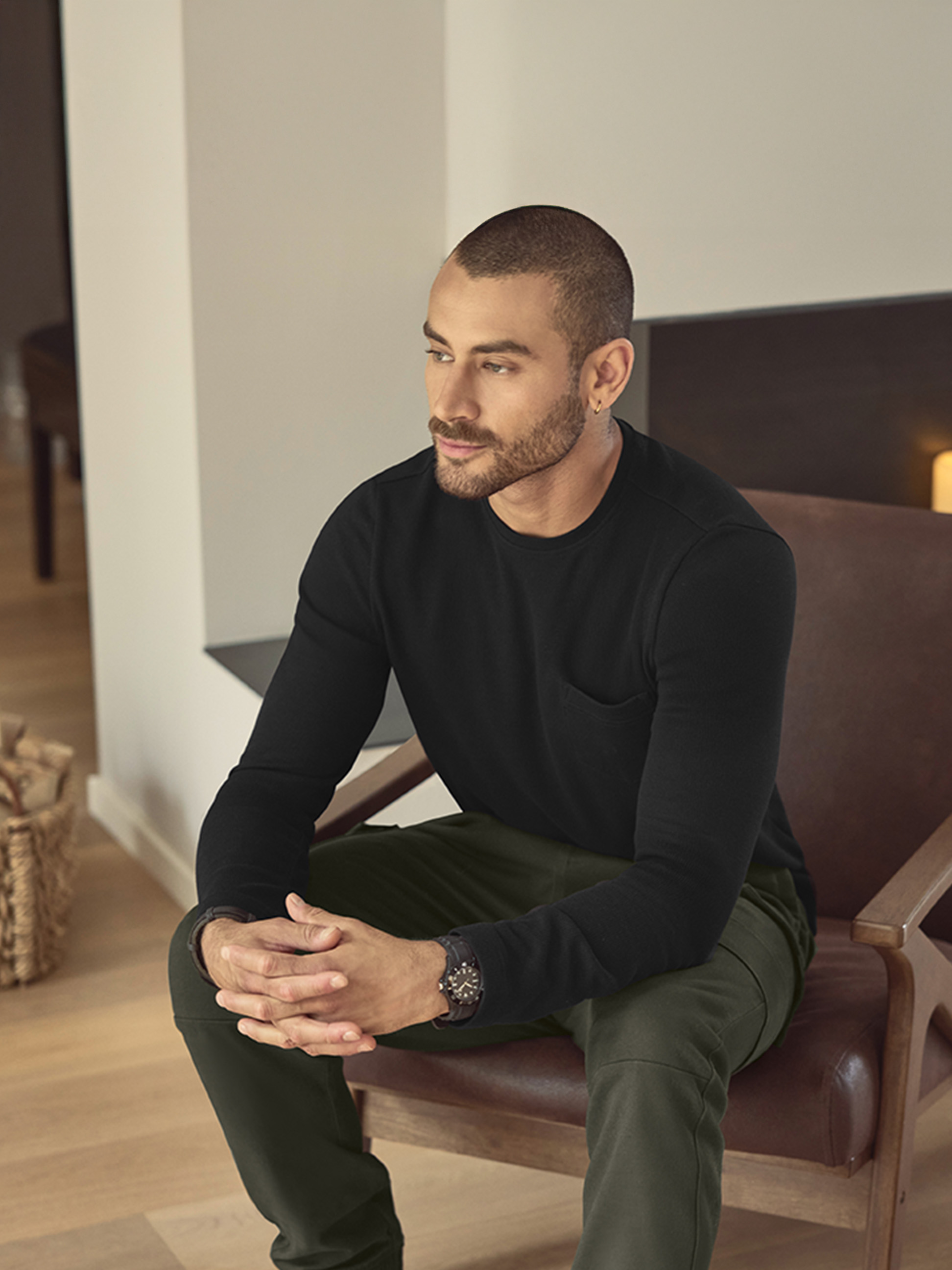 Man in een zwart shirt met lange mouwen en groene broek, zittend op een leren stoel