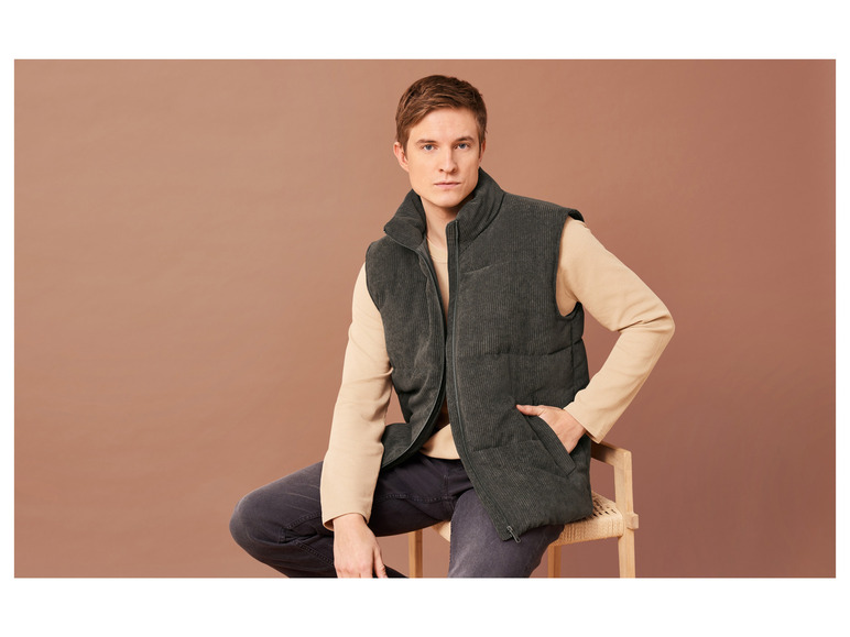 Man draagt een donkergroen corduroy vest en zit op een houten stoel.