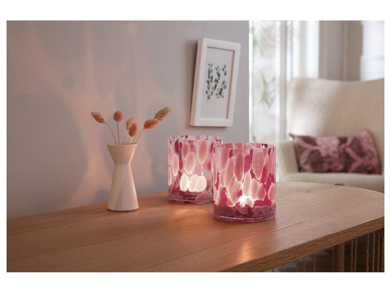 Twee roze decoratieve kaarsen en een vaas met gedroogde bloemen op een houten tafel.