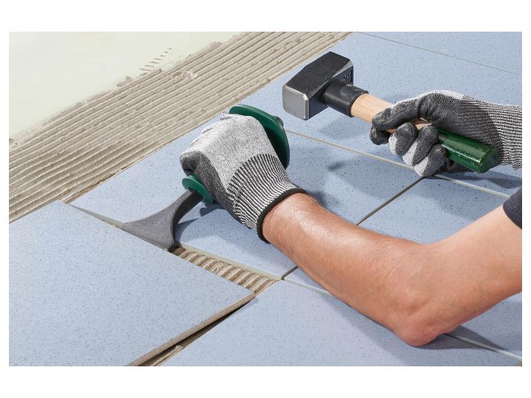 Man legt vloertegels met een hamer en tegelzetgereedschap.