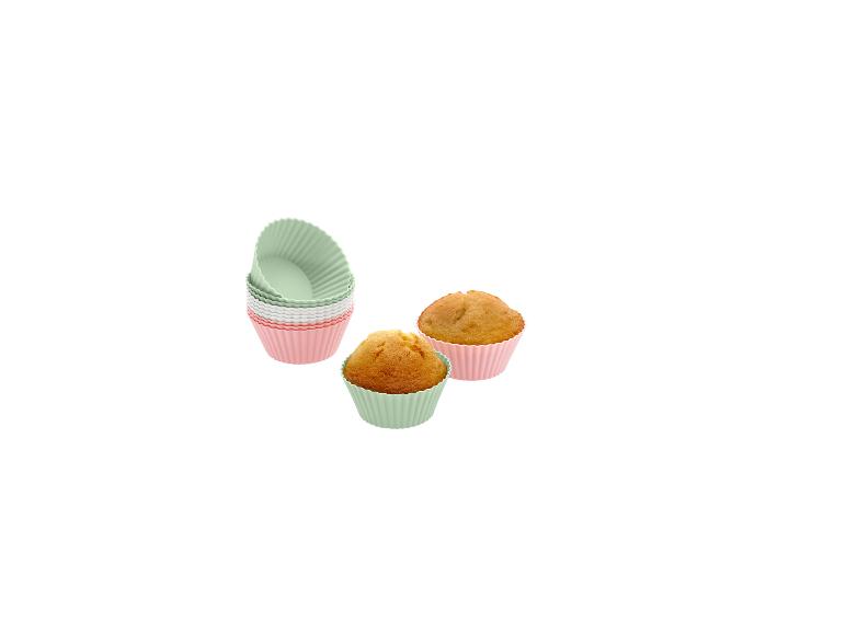Siliconen muffinvormpjes in roze, wit en mintgroen, met twee gebakken muffins.