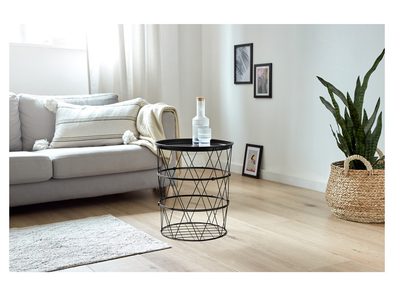 Een zwarte metalen bijzettafel met een glazen vaas en een plant in een rieten mand.