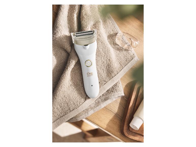 Wit dames scheerapparaat op een beige handdoek, met de tekst 'BEAUTY'.