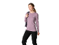 Vrouw in lila shirt met lange mouwen en zwarte broek, met een rugzak op haar schouder.