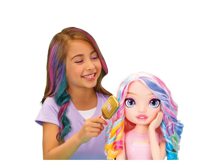 Lachend meisje met gekleurd haar kamt een pop met gekleurd haar