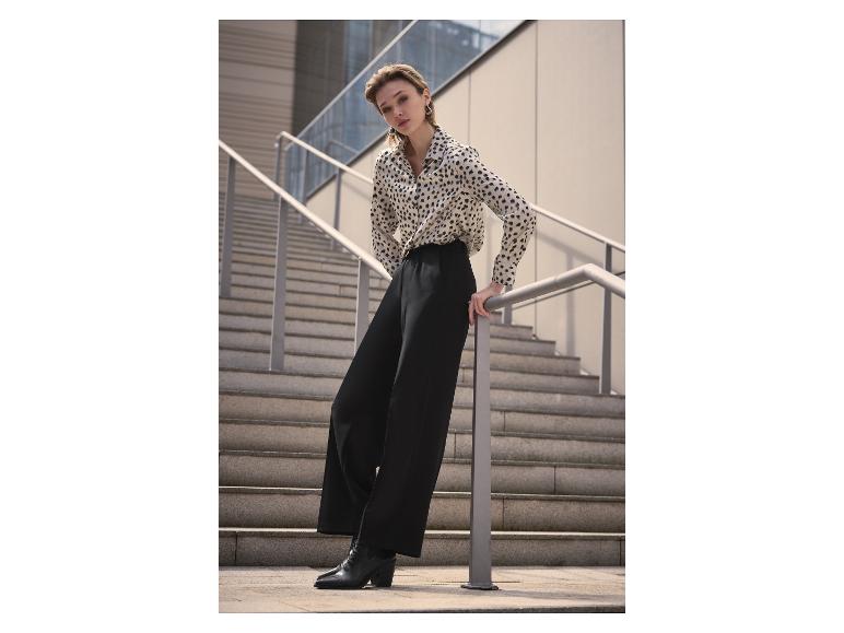 Vrouw in een luipaardprint blouse en zwarte broek, leunend op een trapleuning.