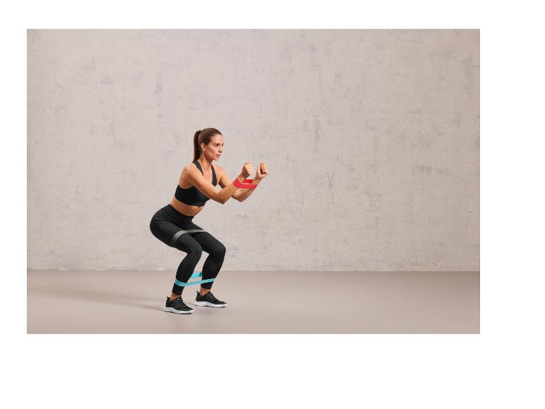 Een vrouw die squats doet met een blauwe en rode weerstandsband.