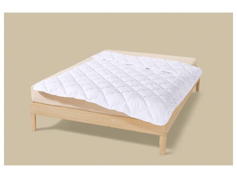 Houten bed met matras en witte gewatteerde matrasbeschermer.