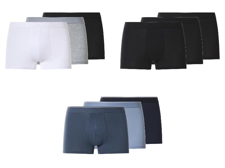 Drie verpakkingen herenboxershorts in wit, grijs, zwart en blauwtinten.