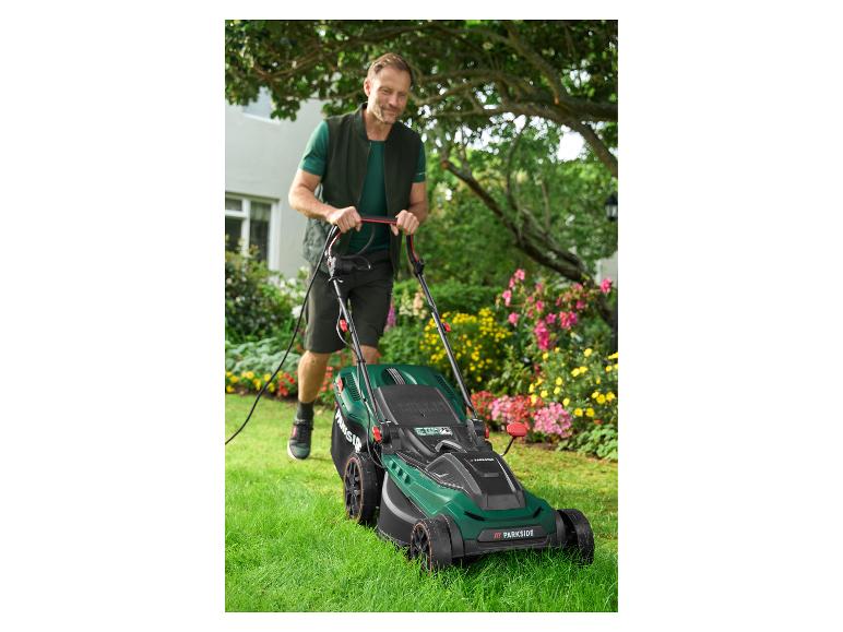 Man maait gazon met een Parkside elektrische grasmaaier in een bloemrijke tuin.