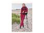 Vrouw in rode wandeljas en broek, rugzak en wandelstokken op het strand.