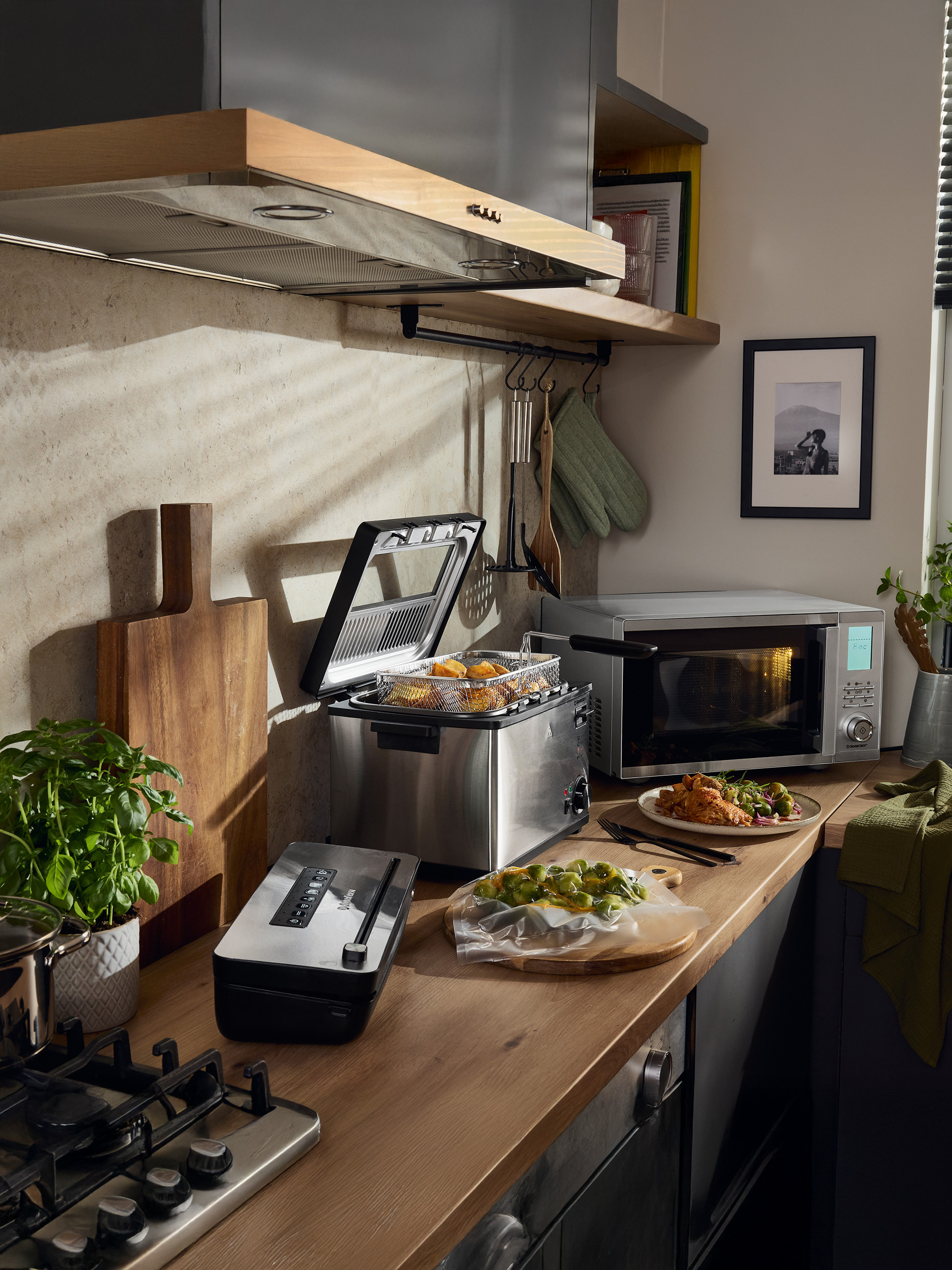Keuken met friteuse, SilverCrest magnetron, vacuümapparaat en bereid voedsel.
