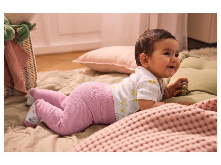 Lachende baby in roze legging en rompertje met giraffes, liggend op de buik.
