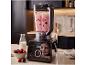 Blender maakt bessensmoothie op aanrecht, met bessen en melk ernaast.