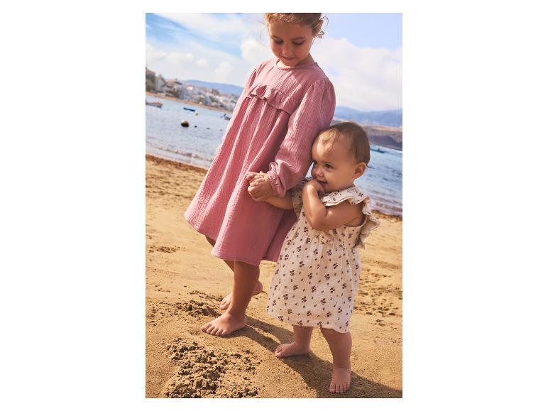 Twee meisjes in zomerjurken op het strand, de oudste houdt de jongste bij de hand.