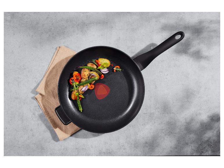 Zwarte koekenpan met geroosterde groenten (aardappelen, okra, paprika, uien) op een beige doek.