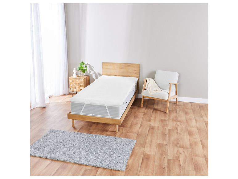 Een wit matrasbeschermer op een houten bedframe met een grijs vloerkleed