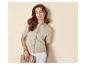 Vrouw in een beige vest met korte mouwen en witte broek, met een clutch.