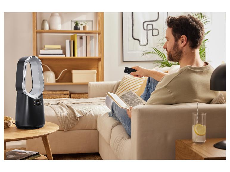 Een man ontspant op de bank en bedient een bladelouse Dyson ventilator met een afstandsbediening.