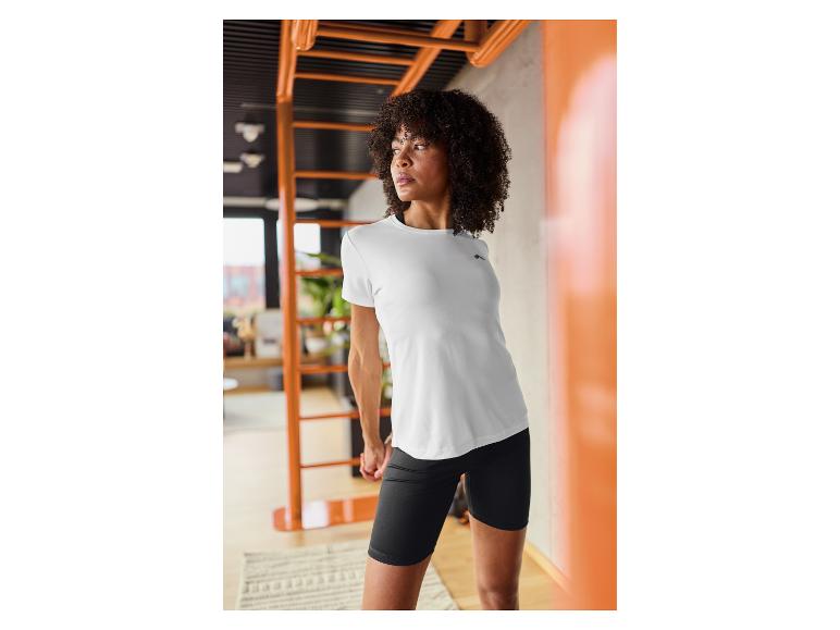 Vrouw in wit T-shirt en zwarte korte broek, aan het stretchen in een sportschool.