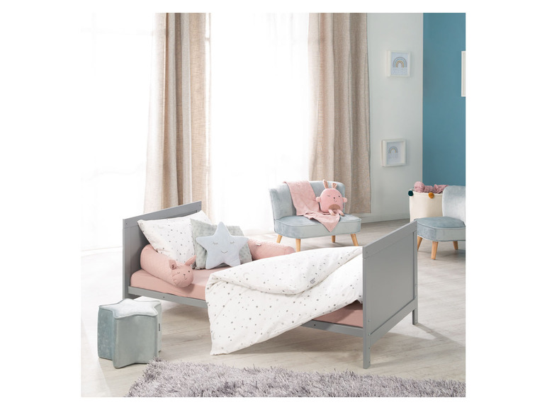 Een grijs kinderbed met roze beddengoed en kussens met sterren.