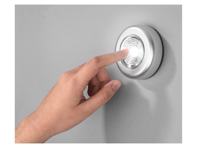 Hand drukt op een rond zilveren LED-lampje aan een grijze muur