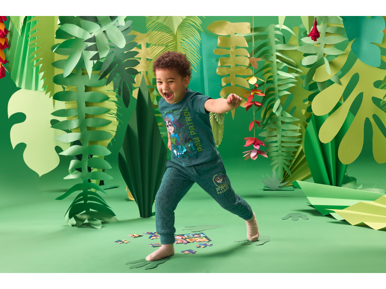 Kind speelt in een groene jungle-omgeving, gekleed in een Paw Patrol-outfit.