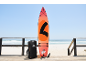 Oranje paddleboard met accessoires en tas op een houten vlonder bij het strand.