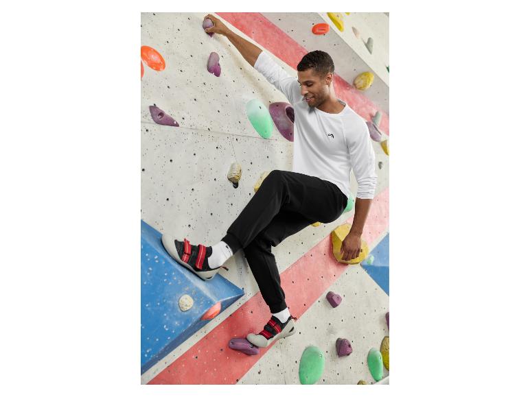 Man in wit shirt met lange mouwen en zwarte joggingbroek aan het boulderen.