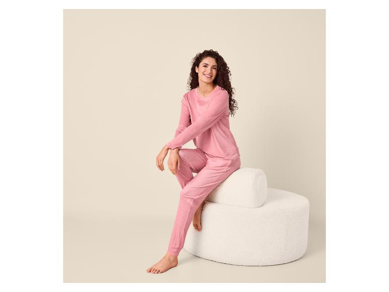Vrouw in roze pyjama met stippen zit lachend op een witte kruk.