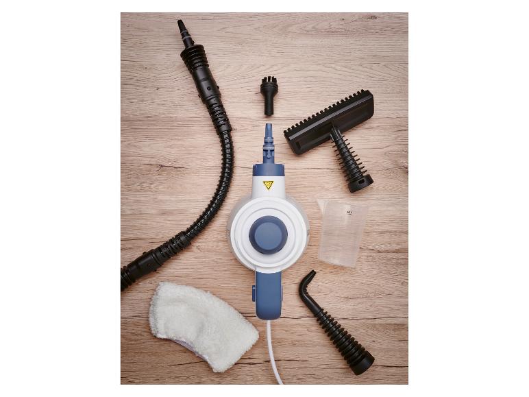 Handstoomreiniger met diverse opzetstukken, maatbeker en reinigingsdoek op een houten ondergrond.