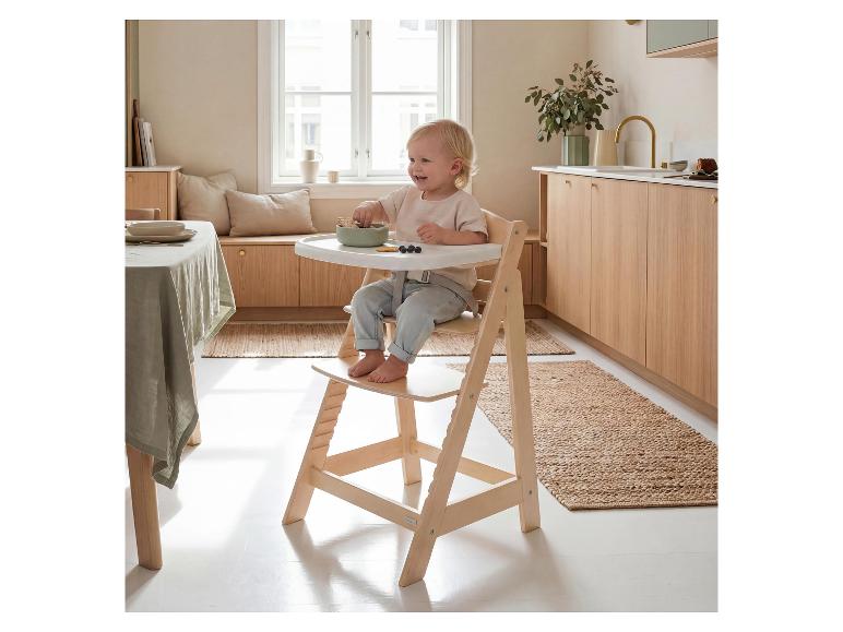 Lachende peuter in houten kinderstoel, eet koekjes en bosbessen in een lichte keuken.