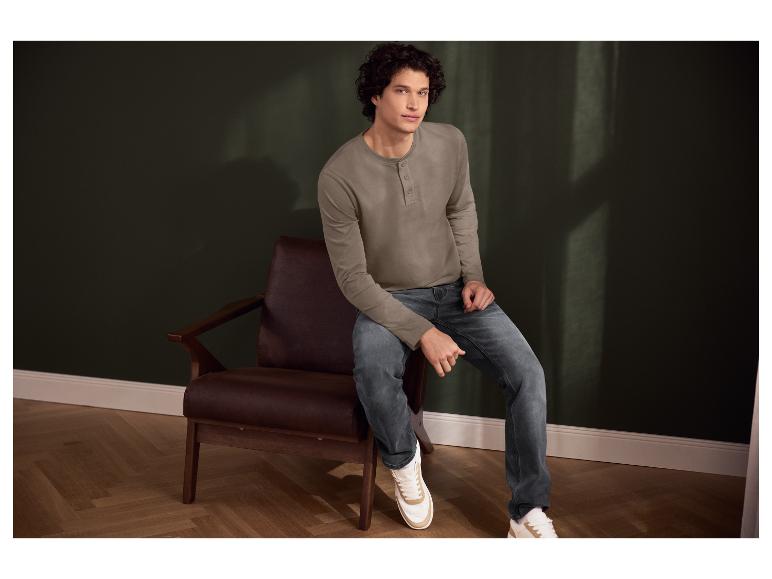 Man met krullend haar, longsleeve en jeans zit in een fauteuil.