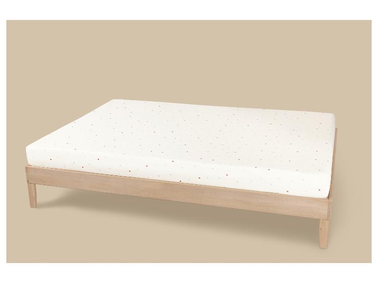 Houten bed met een wit matras met kleurrijke stippen op een beige achtergrond.