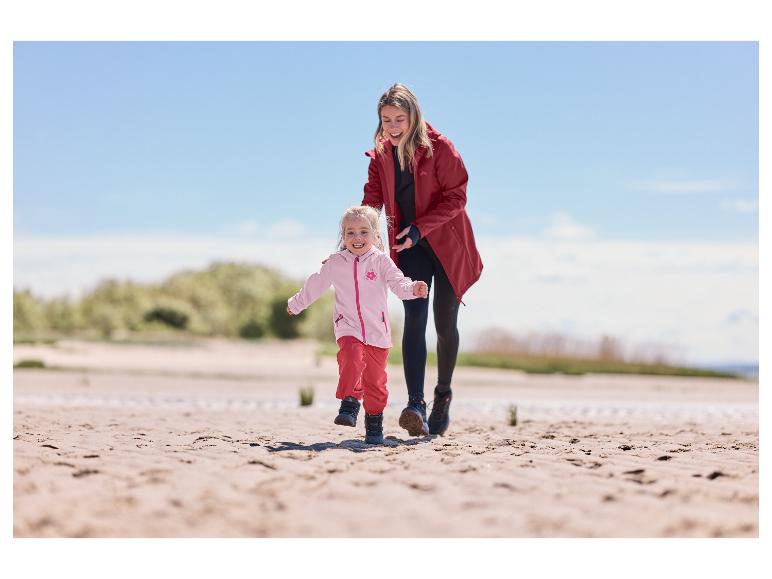 Meisje in een roze LUPILU softshelljas rent op het strand met haar moeder.