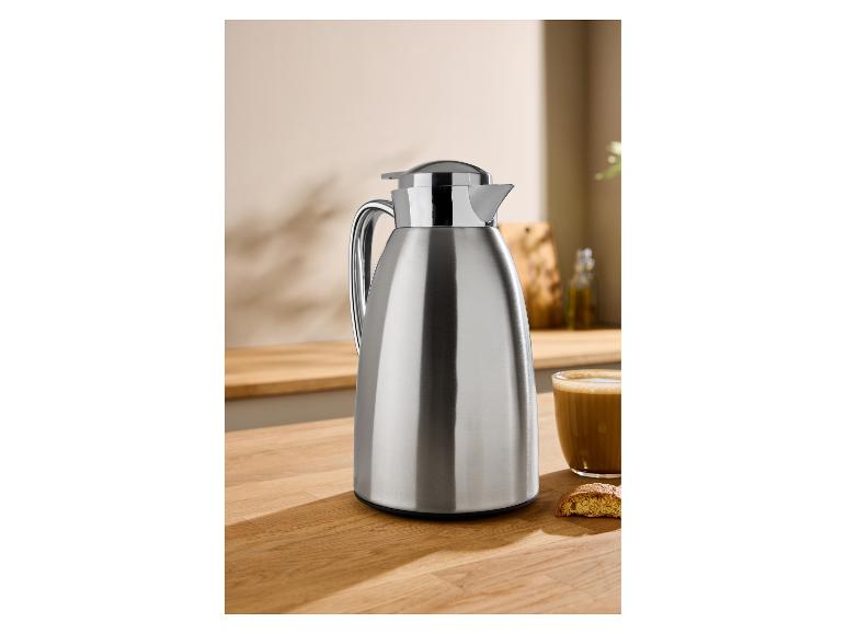 Roestvrijstalen thermoskan op een houten aanrecht met koffie en een koekje.