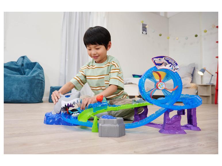 Een jongen speelt met een Hot Wheels Shark Cyclone speelset op de vloer.