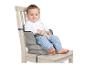 Een lachende baby zit in een grijze zitverhoger vastgemaakt aan een houten stoel.