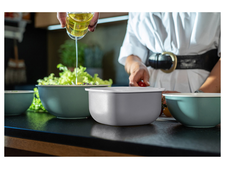 Een persoon giet olie in een groene kom met sla.